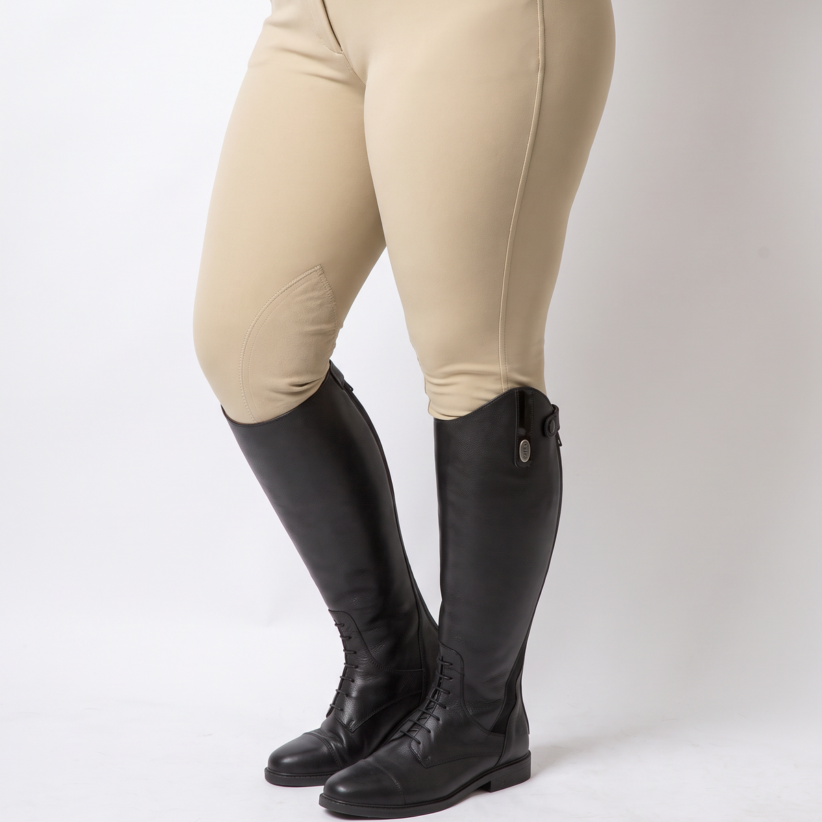 Beige equestrian riding breeches with a blue leather belt, modelled with black plus size riding boots and a white shirt against a light grey studio background.